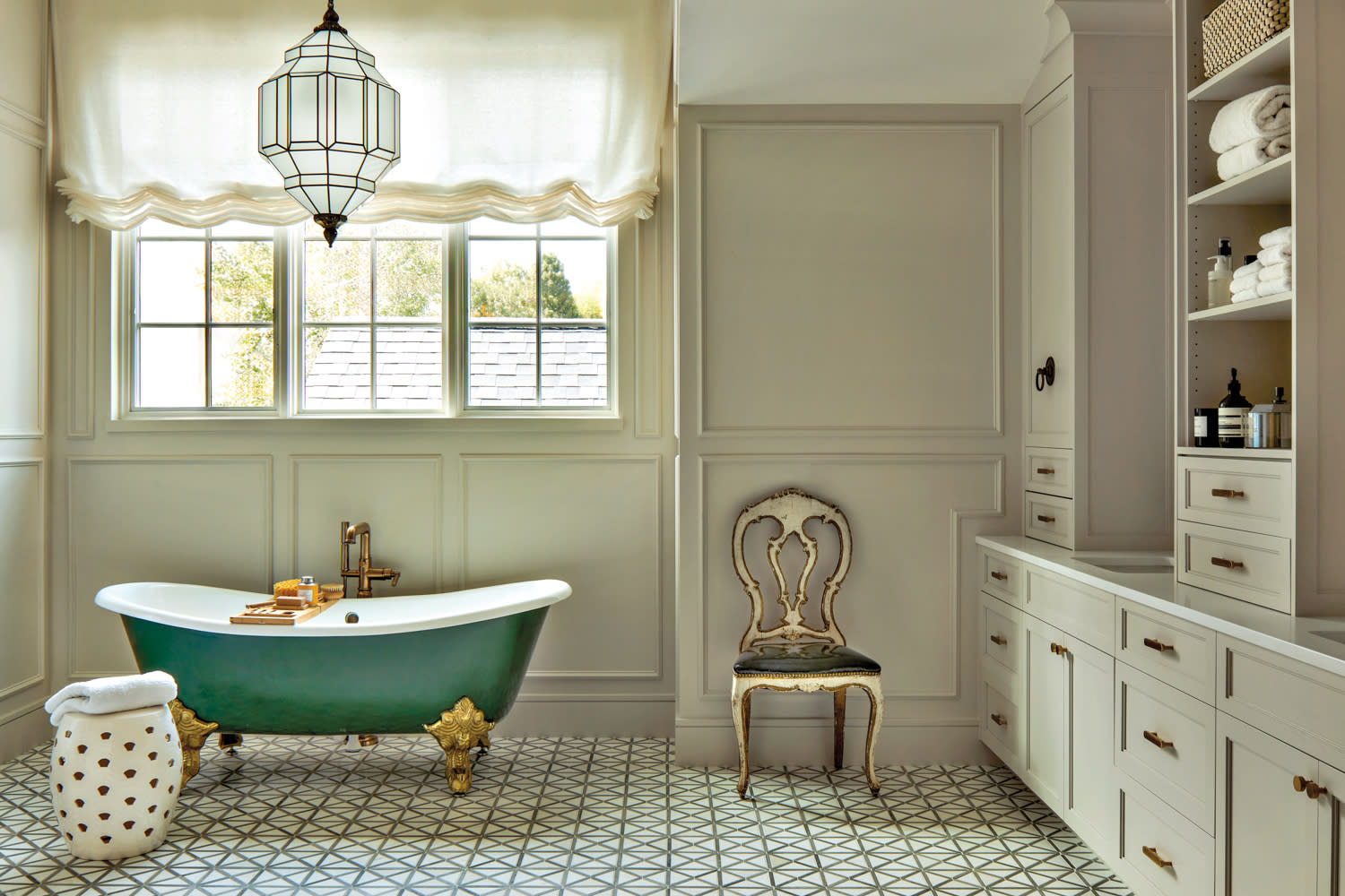 A cream colored bathroom with tile floors and a freestanding tub painted hunter green