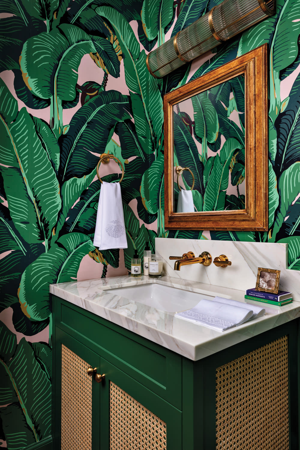 powder room with green banana leaf-print wallpaper, white sink and wood-framed mirror in home by Sara McCann